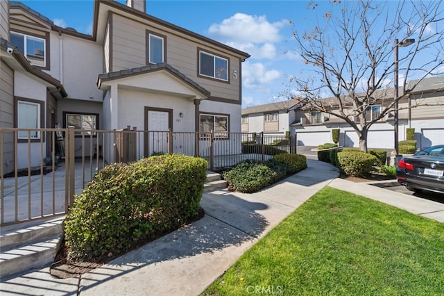 townhome / multi-family property featuring a residential view, a fenced front yard, and stucco siding