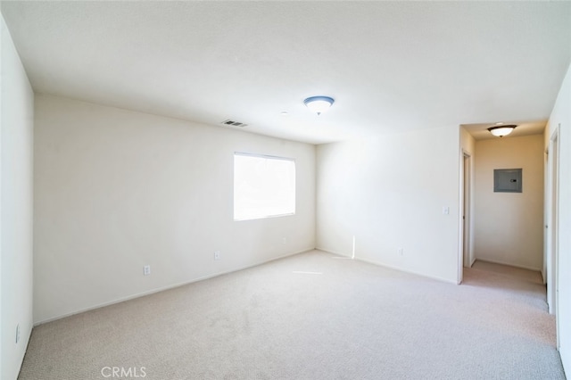 empty room with electric panel, visible vents, and light carpet