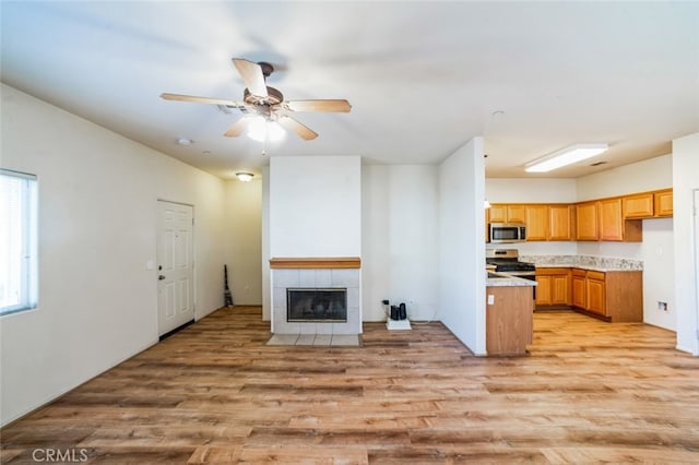 kitchen featuring light wood-style flooring, a fireplace, ceiling fan, light countertops, and appliances with stainless steel finishes