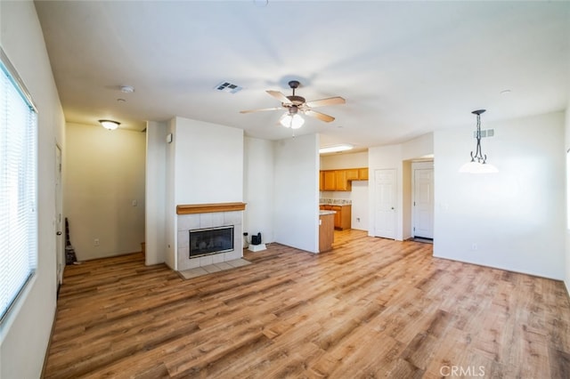 unfurnished living room with light wood finished floors, visible vents, a tiled fireplace, and ceiling fan