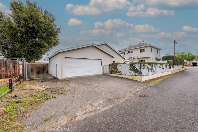 view of front of house with fence, aphalt driveway, stucco siding, a garage, and a gate