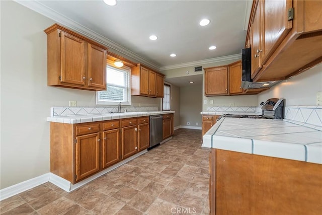 kitchen with stainless steel appliances, tile counters, brown cabinetry, and crown molding