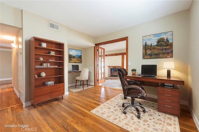 office space with visible vents, baseboards, a fireplace, and light wood finished floors