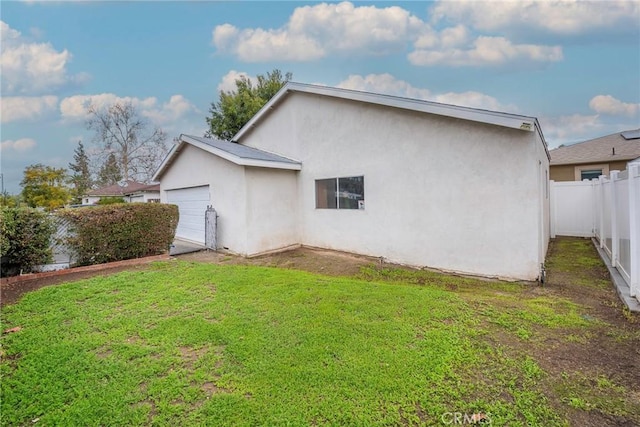 rear view of house featuring a garage, fence, a lawn, and stucco siding