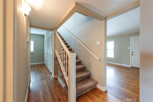 stairs featuring baseboards, plenty of natural light, wood finished floors, and ornamental molding