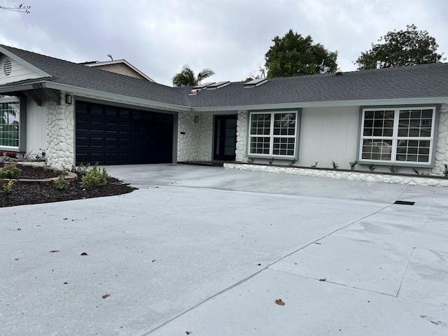 ranch-style home featuring stone siding, an attached garage, and driveway