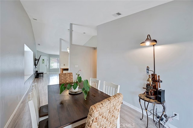 dining room featuring lofted ceiling, light wood-style flooring, visible vents, and baseboards