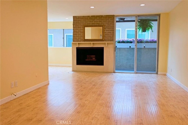 unfurnished living room with a brick fireplace, baseboards, a wall of windows, recessed lighting, and wood finished floors