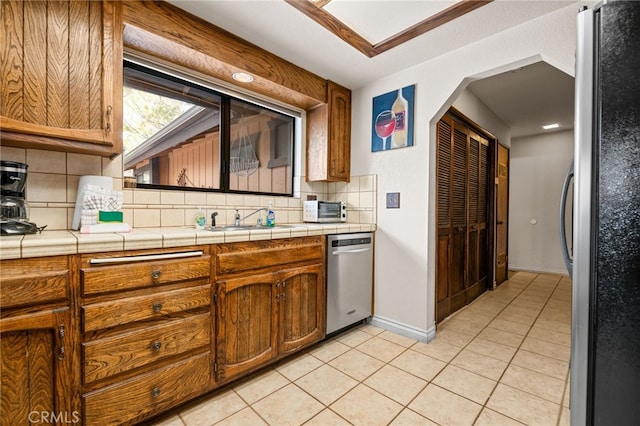 kitchen with brown cabinets, a sink, backsplash, stainless steel appliances, and light tile patterned flooring