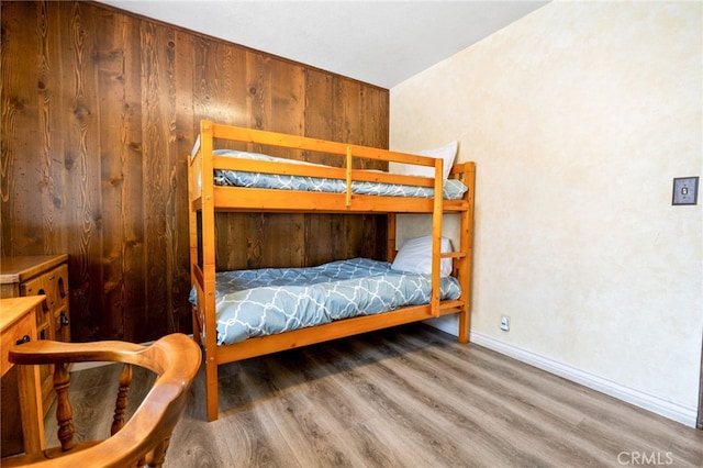 bedroom with wood finished floors, baseboards, and wood walls