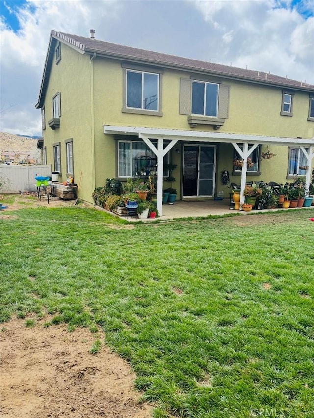 rear view of property featuring a patio area, a lawn, and stucco siding