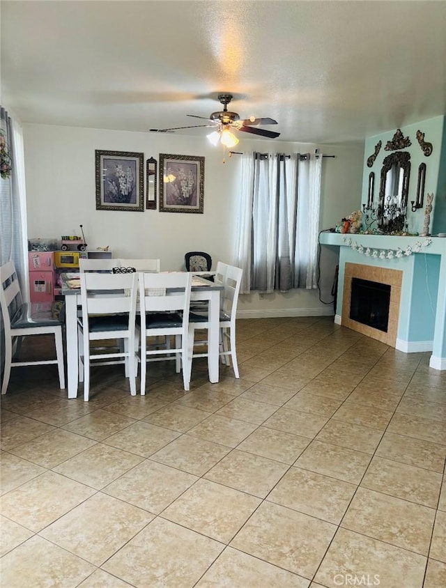 dining space with light tile patterned flooring, a fireplace, baseboards, and a ceiling fan