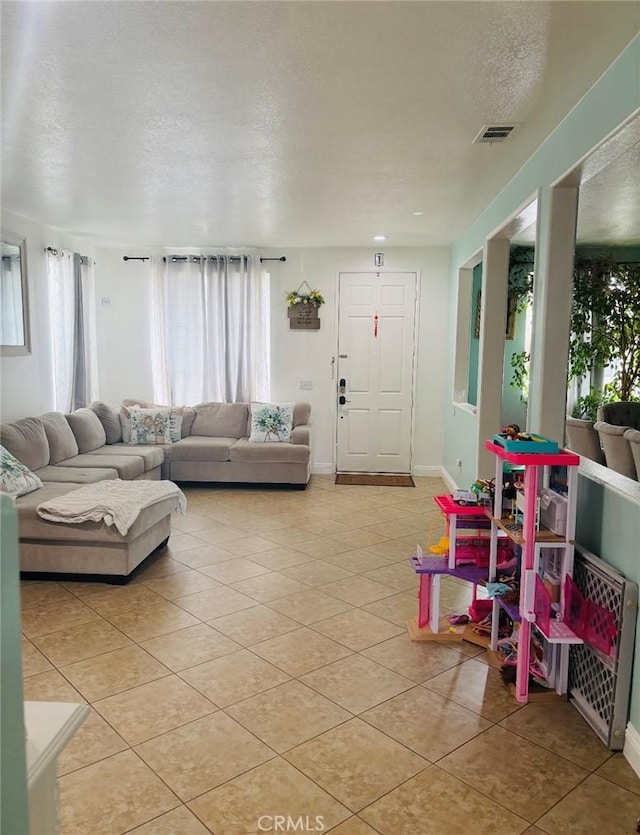 living area with light tile patterned floors, visible vents, baseboards, and a textured ceiling