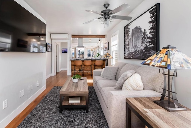 living area with baseboards, a wall mounted air conditioner, a ceiling fan, and wood finished floors