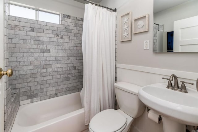 bathroom featuring a sink, shower / bathtub combination with curtain, toilet, and a wainscoted wall