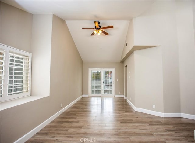 empty room with baseboards, high vaulted ceiling, wood finished floors, and a ceiling fan