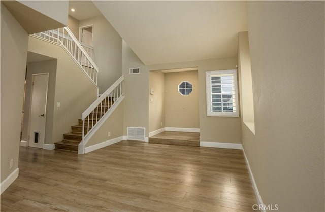 entrance foyer with visible vents, wood finished floors, baseboards, a towering ceiling, and stairs