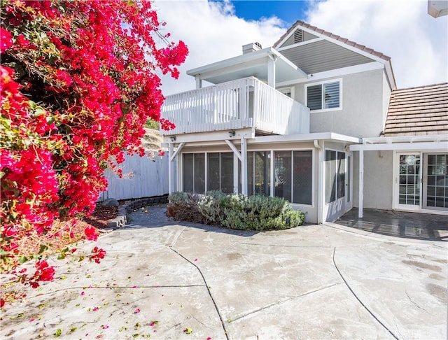 rear view of house featuring stucco siding, a sunroom, a balcony, a chimney, and a patio area