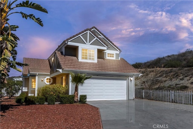 view of front of property featuring a tile roof, fence, a garage, and driveway