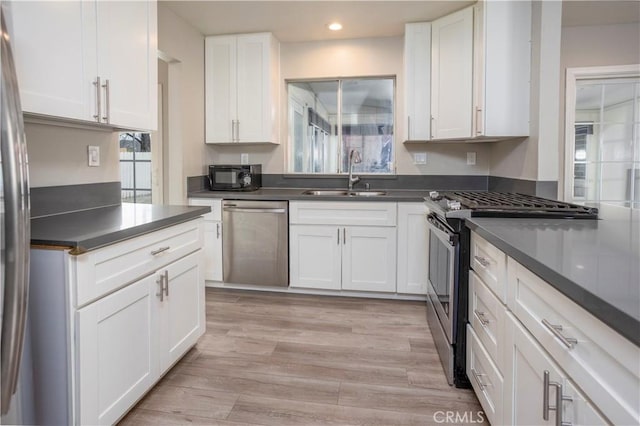 kitchen featuring a sink, stainless steel appliances, dark countertops, and white cabinetry