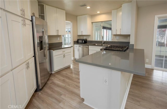 kitchen featuring light wood-style flooring, appliances with stainless steel finishes, a peninsula, and a sink