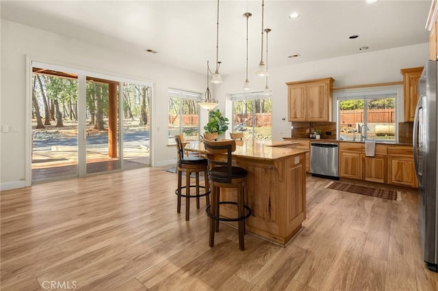 13725 Nimshew Rd, Magalia, CA 95954 - kitchen featuring a breakfast bar area, a kitchen island, appliances with stainless steel finishes, decorative light fixtures, and light wood-type flooring