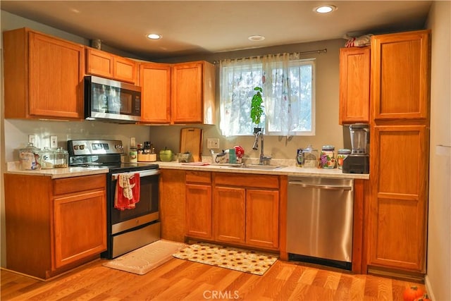 kitchen with a sink, light wood-style floors, appliances with stainless steel finishes, and light countertops
