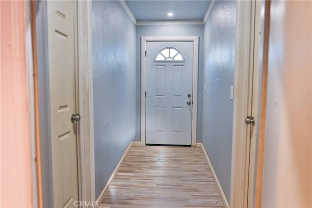 doorway featuring light wood-type flooring, baseboards, ornamental molding, and a textured wall