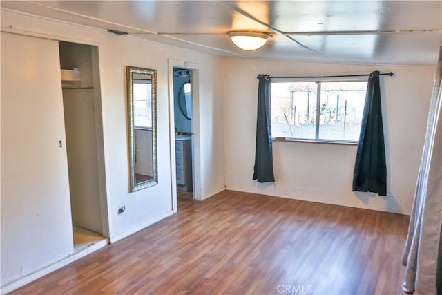 unfurnished bedroom with a closet, wood finished floors, and stacked washing maching and dryer