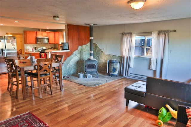 dining area featuring a wood stove, light wood-style floors, and a baseboard radiator