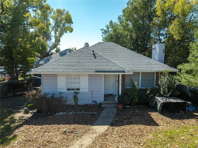 view of front of home featuring a chimney, roof with shingles, and fence