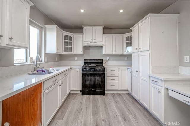 kitchen featuring a sink, white cabinetry, under cabinet range hood, and black gas stove