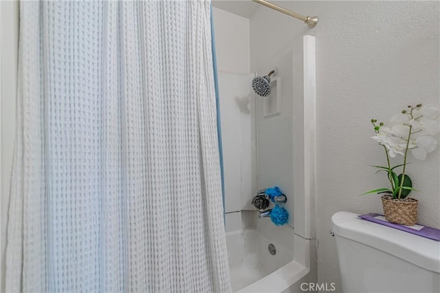 bathroom with toilet, shower / bath combo with shower curtain, and a textured wall