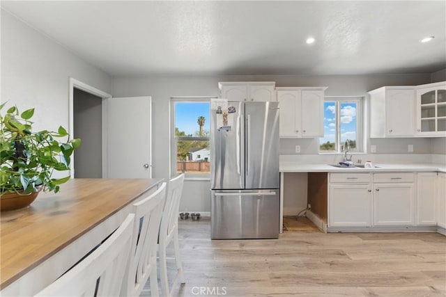 kitchen with light wood-type flooring, recessed lighting, freestanding refrigerator, white cabinets, and a sink