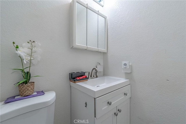 bathroom with toilet, vanity, and a textured wall