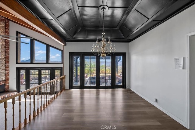 foyer featuring wood finished floors, baseboards, french doors, a raised ceiling, and a notable chandelier