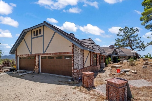 view of side of home with an attached garage, a chimney, driveway, and stucco siding