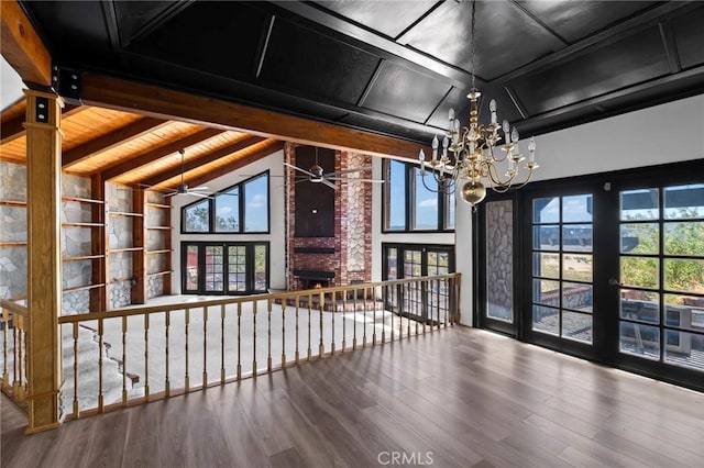 interior space featuring beamed ceiling, a brick fireplace, wood finished floors, and ceiling fan with notable chandelier