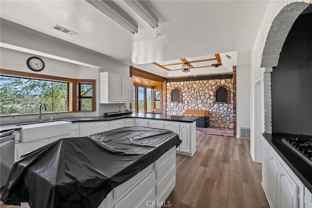 kitchen featuring dark countertops, visible vents, a peninsula, wood finished floors, and a sink