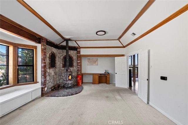 unfurnished living room with baseboards, visible vents, lofted ceiling, a wood stove, and light carpet