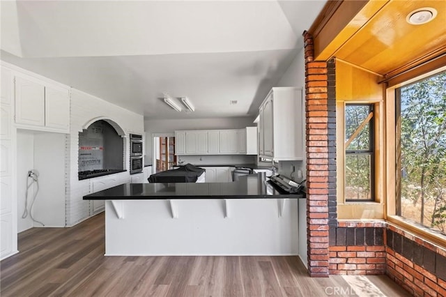 kitchen with dark countertops, a peninsula, dark wood finished floors, and white cabinetry