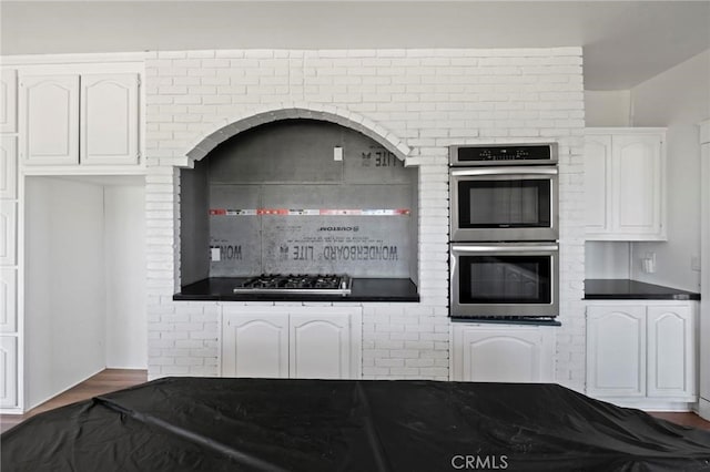 kitchen with dark countertops, dark wood-style floors, gas stovetop, double oven, and white cabinets