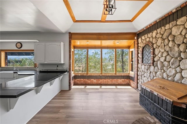 kitchen featuring dark countertops, a kitchen bar, wood finished floors, white cabinets, and a sink