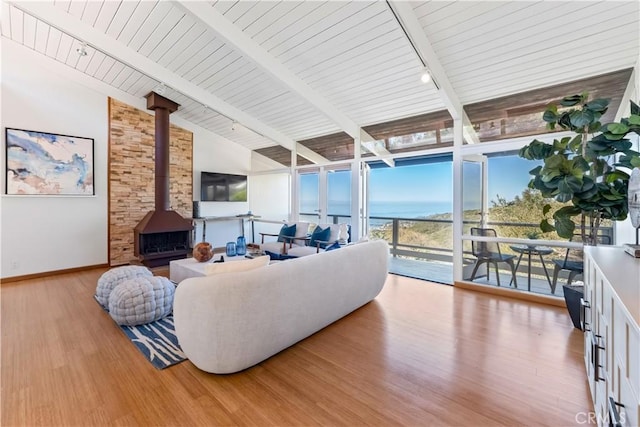 living area with beam ceiling, track lighting, wood finished floors, floor to ceiling windows, and a wood stove