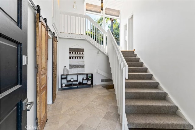 interior space featuring baseboards, visible vents, stairs, a towering ceiling, and a barn door