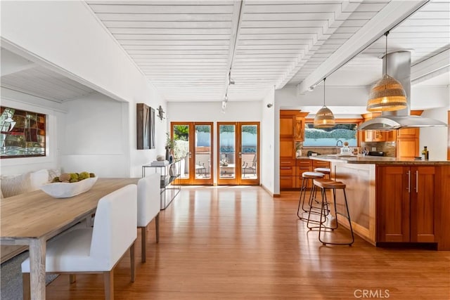 dining room with beamed ceiling, light wood-style floors, and french doors