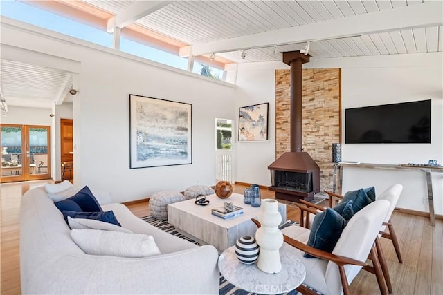 living room featuring beam ceiling, a wood stove, wood finished floors, and track lighting