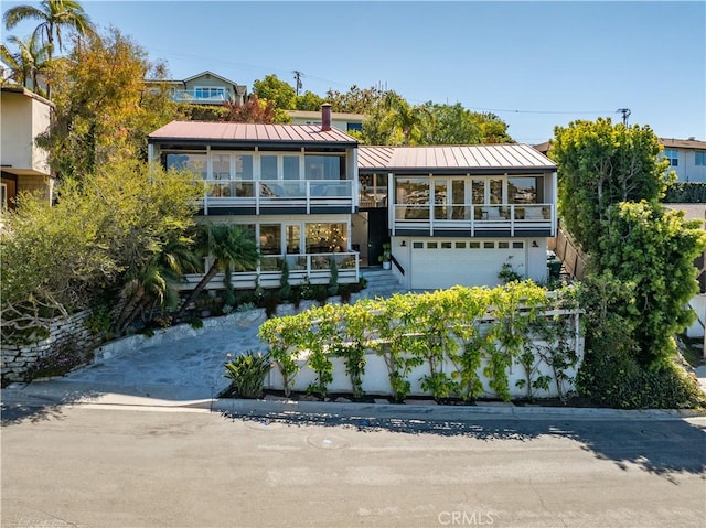 rear view of property with a garage, a standing seam roof, metal roof, a balcony, and stairs