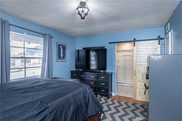 bedroom with ensuite bath, a barn door, wood finished floors, and a textured ceiling