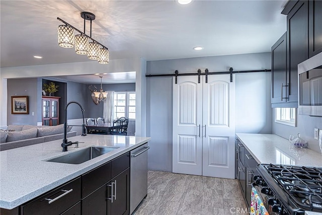 kitchen featuring pendant lighting, a barn door, a notable chandelier, stainless steel appliances, and a sink